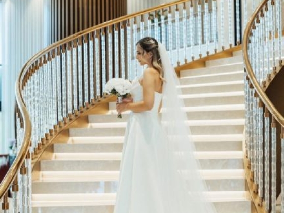 Elegant bride holding flowers on a grand staircase.