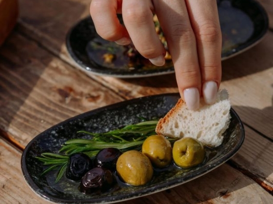 A hand picks up bread near olives and herbs on a plate.