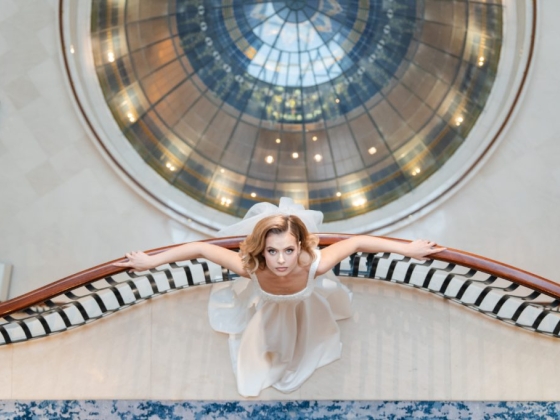 A bride in a white dress poses elegantly on a staircase.