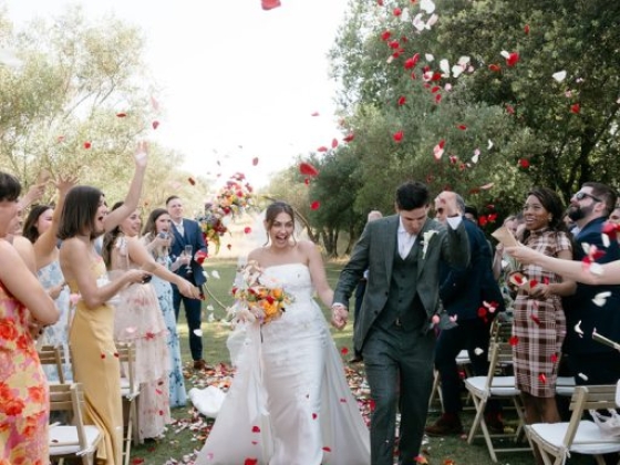 Newlyweds walk joyfully amidst flower petals and guests.