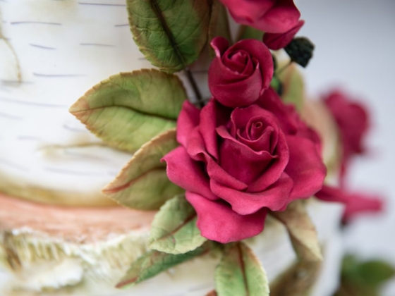 Close-up of a cake featuring red roses and green leaves.