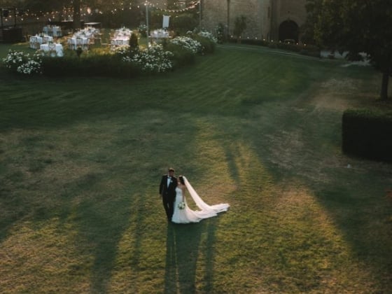 A wedding couple strolls on a lawn with tables set for a celebration.