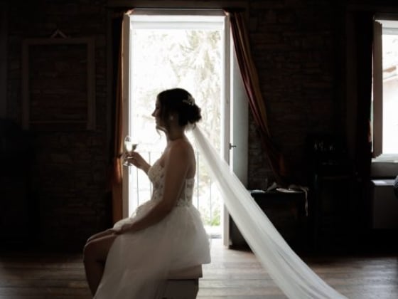A bride sits gracefully, sipping champagne in a cozy room.