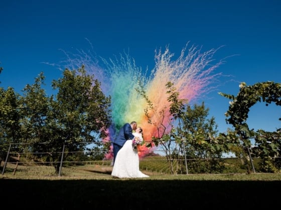 Couple celebrating with rainbow smoke during outdoor wedding.