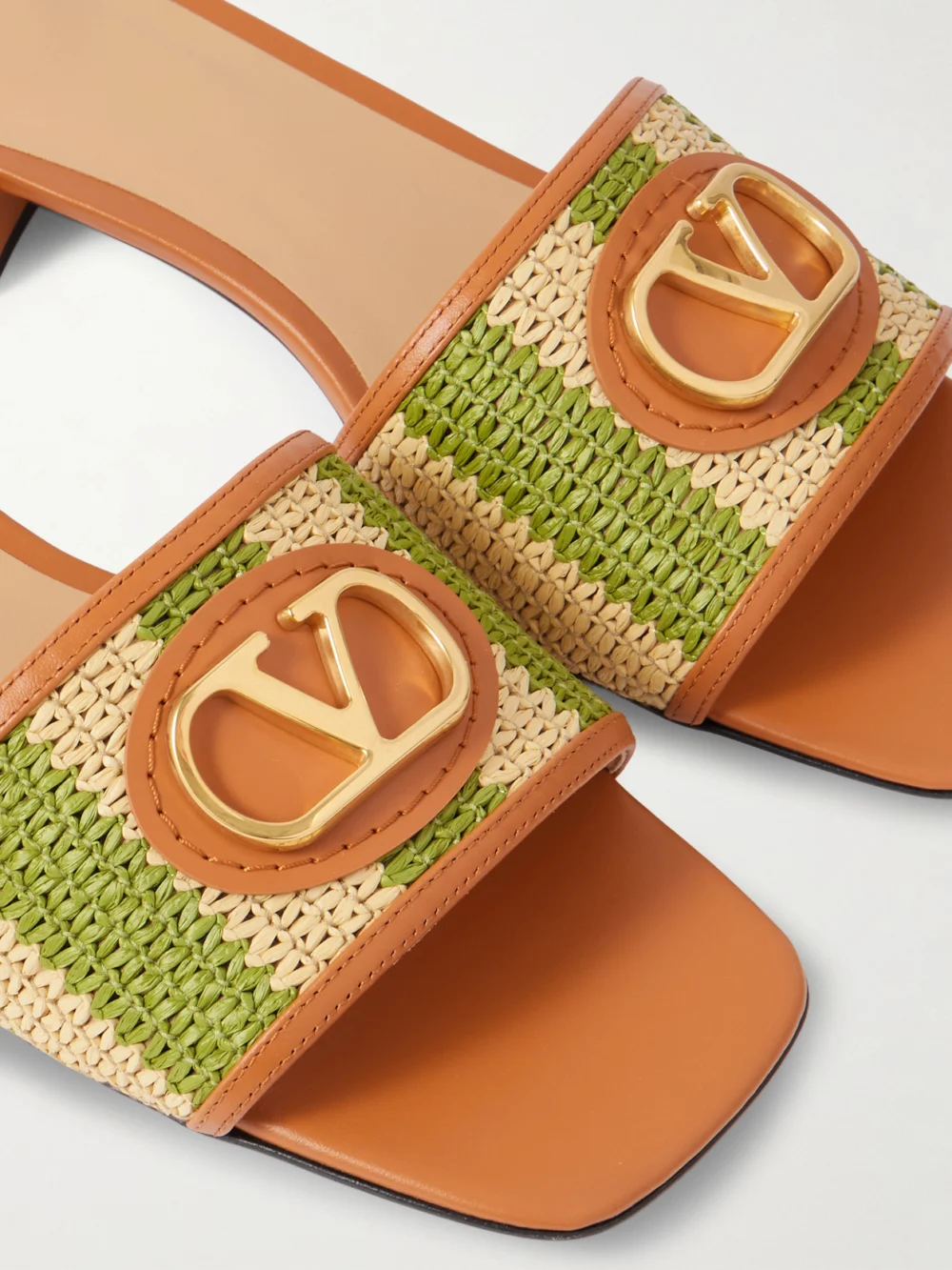 Close-up detail of the Valentino Garavani Vlogo Embellished Leather-trimmed Striped Raffia Slides
