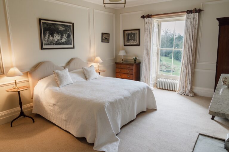 A cream bedroom with a double bed, framed prints and a sash window looking onto the garden, Birdsall House