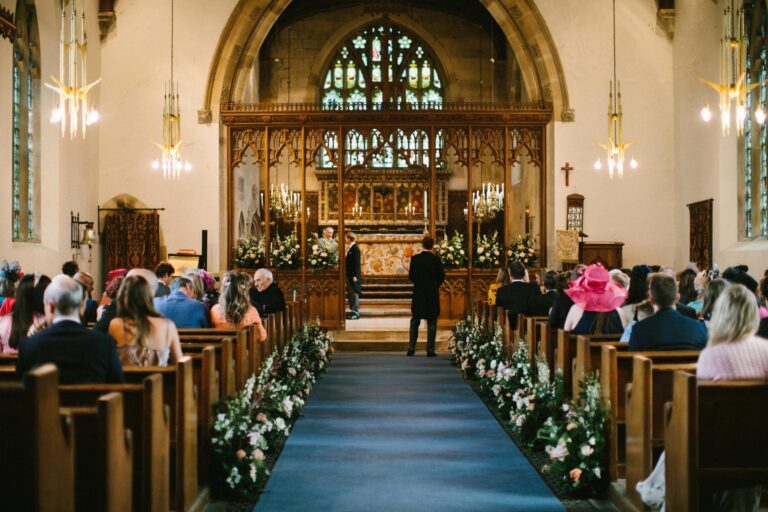 Guests in the pews of St Mary's Church, with flowers lining the aisle to the carved screen and stained glass window, Birdsall House