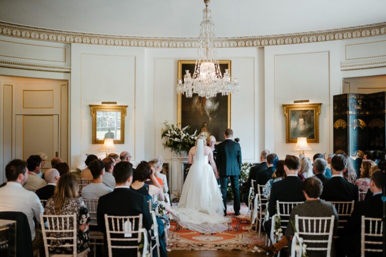 A ceremony in the Oval Room, with guests seated beneath a crystal chandelier and a family portrait, Birdsall House