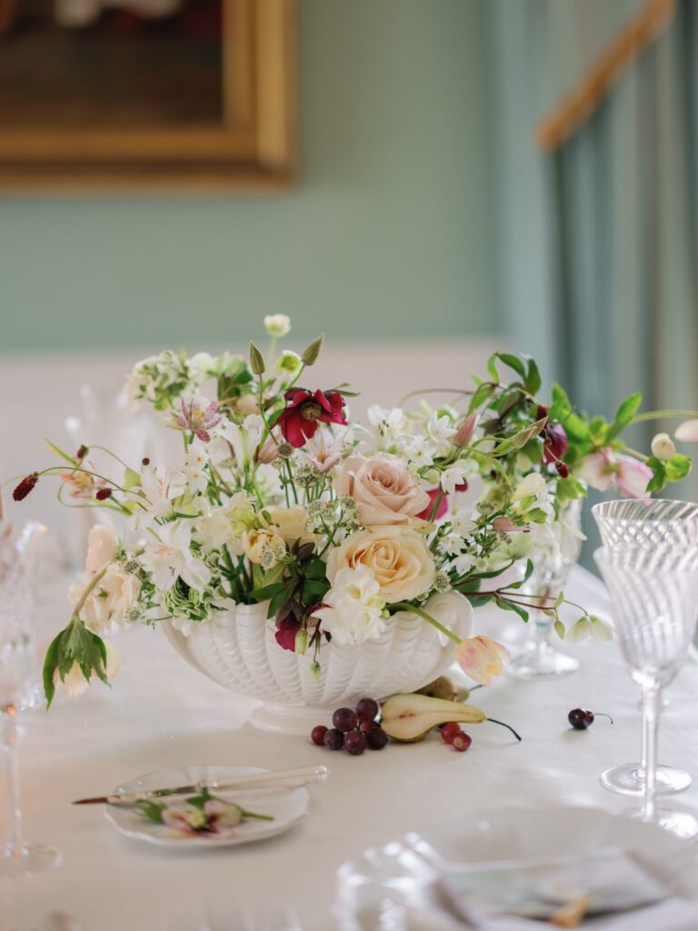 A centrepiece of garden roses and white flowers on a wedding table, with cut-glass goblets, Birdsall House