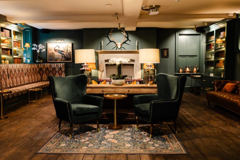 The Old Kitchens lounge with green panelling, a stone fireplace with antlers, velvet armchairs and banquette seating, Birdsall House