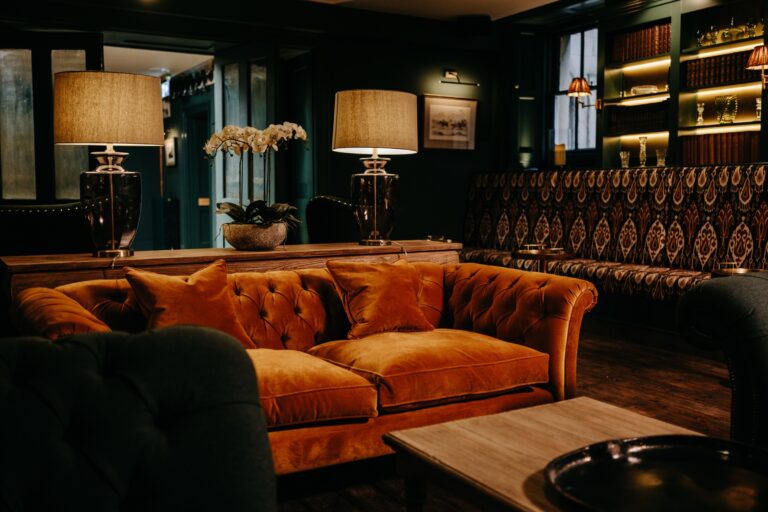 Rust velvet Chesterfield sofas and bookshelves lit from within in The Old Kitchens, Birdsall House