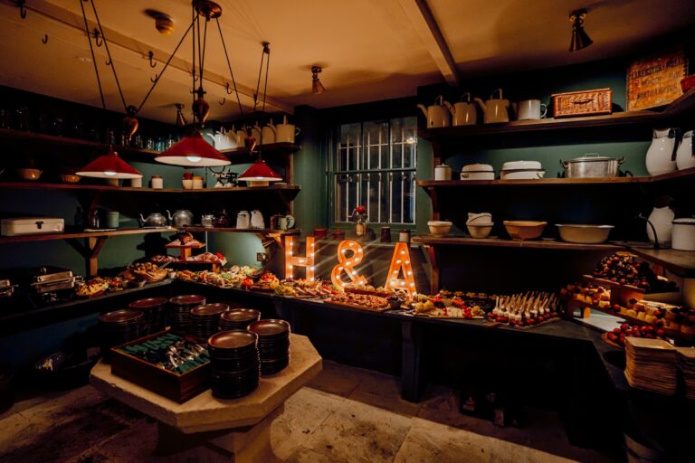 The Pantry in The Old Kitchens laid with a late-night grazing spread under enamel lamps and a light-up H & A sign, Birdsall House