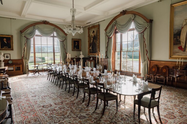 The Dining Room with a long mahogany table, arched windows over the lawns and a patterned rug, Birdsall House