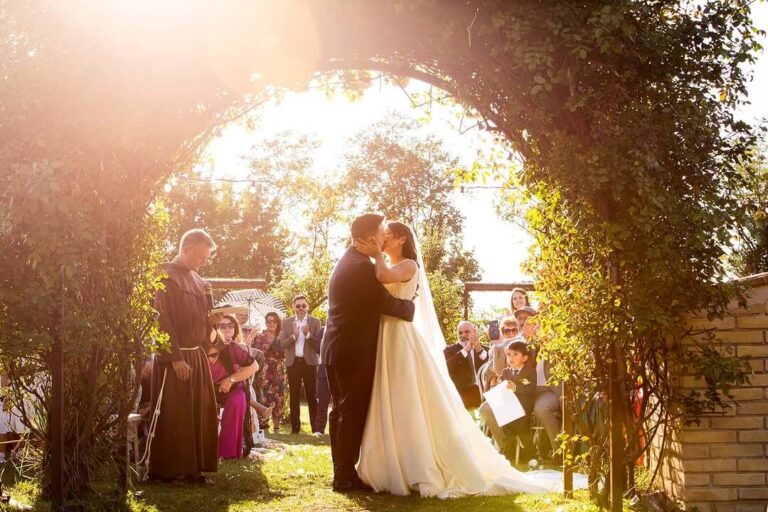 A ceremony under a planted arch in the gardens, with guests gathered around the couple, Borgo Antichi Orti Assisi