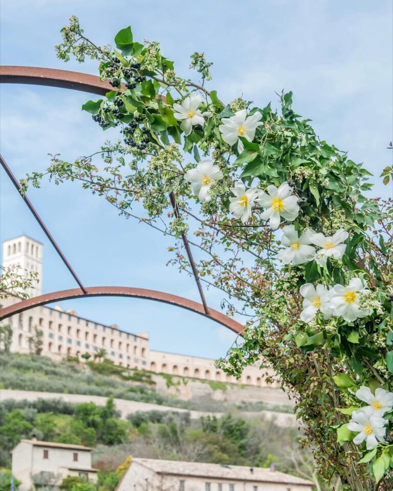 A flowering iron arch in the gardens, framing the Basilica of San Francesco, Borgo Antichi Orti Assisi