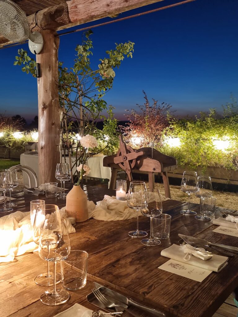A table laid under the wooden pergola at night, with the lights of the valley beyond, Borgo Antichi Orti Assisi