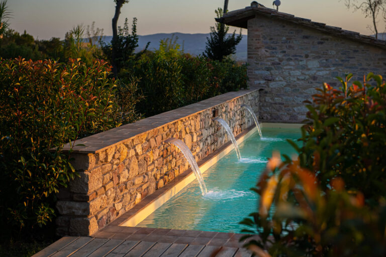 Water spouting from a stone wall into a lit basin in the gardens at dusk, Borgo Antichi Orti Assisi