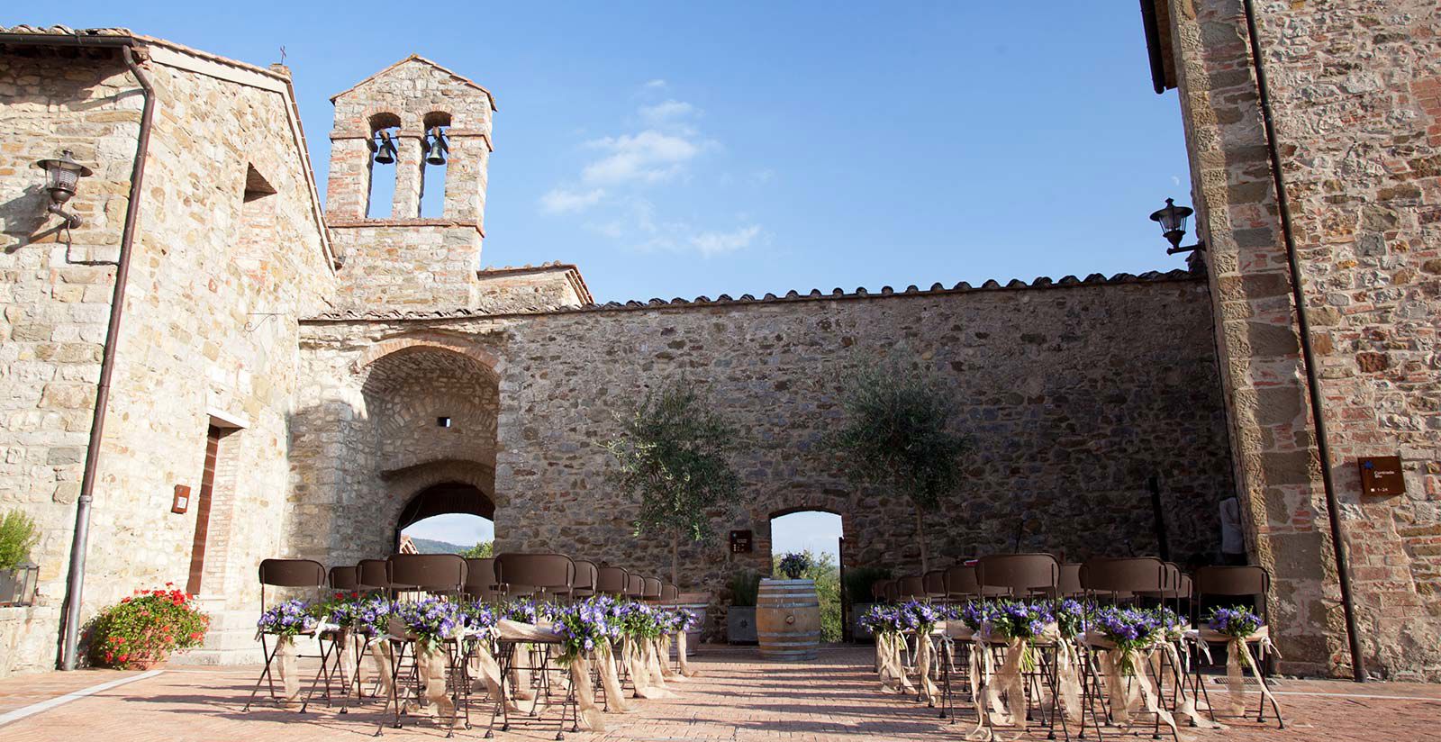 Ceremony chairs set out within the walls below the church bell tower at Castel Monastero