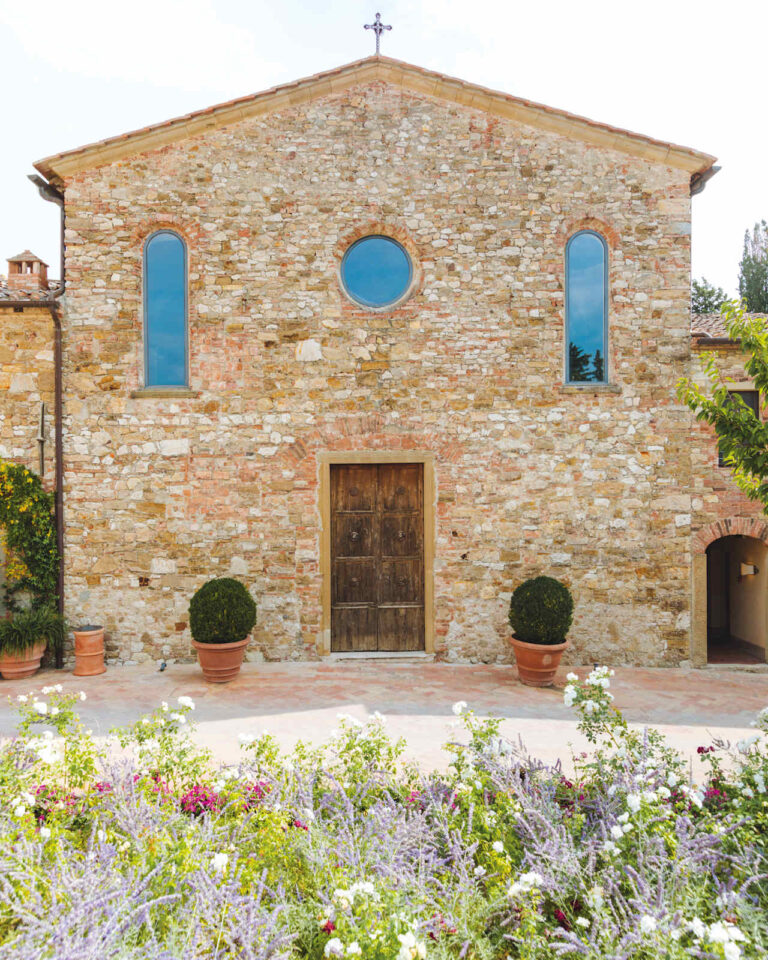 Stone facade of the San Tommaso church with a rose window and potted box trees, Castello di Casole