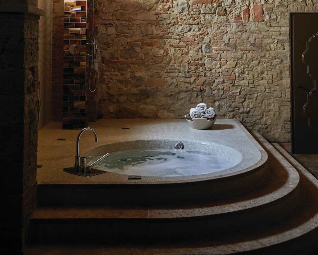 Stone-walled room with a round mosaic tub at the Essere Spa, Castello di Casole