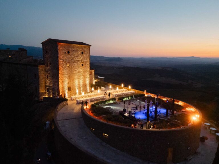 Dinner on the lit round terrace below the tower at dusk, Castello di Velona Resort