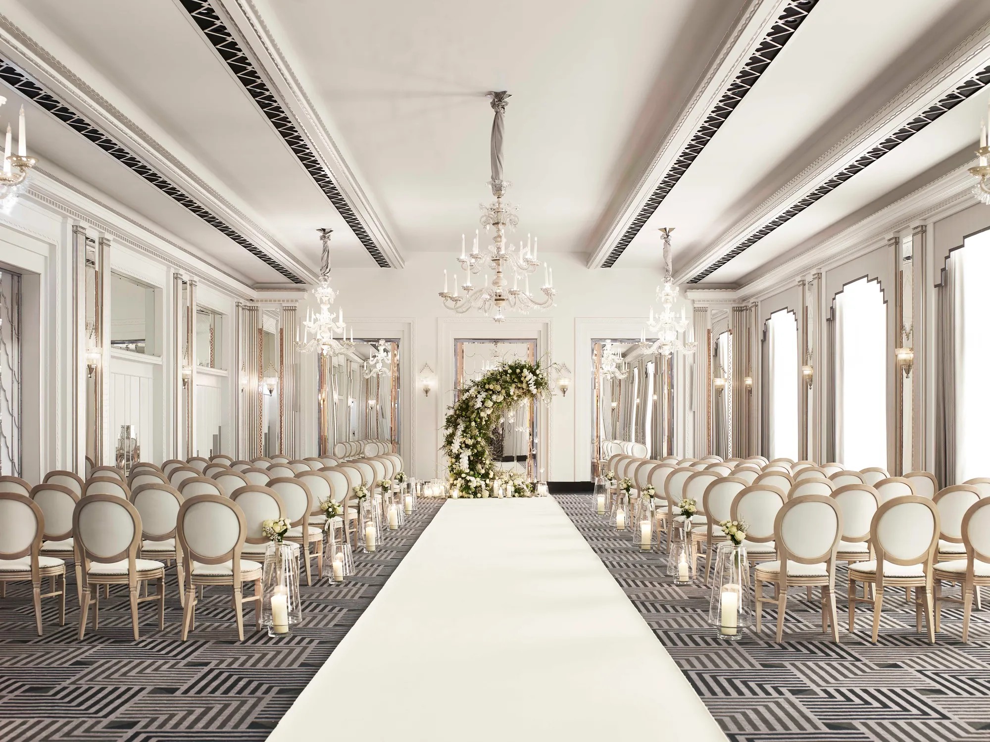 The Ballroom laid out for a ceremony, with rows of chairs either side of a white aisle and a floral arch, Claridge's