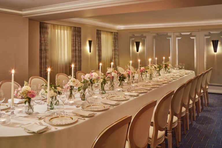 A long candlelit table with flowers laid for dinner in the Highgrove Room, Claridge's