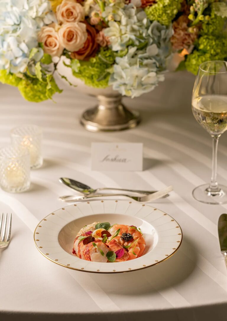 A plated course beside a name card, wine glass and a bowl of garden flowers, Claridge's