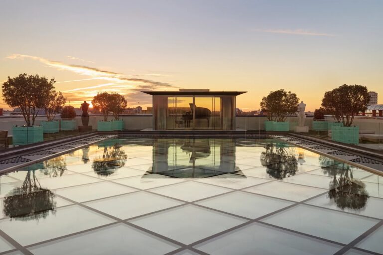 The rooftop pool of The Penthouse at sunset, with trees in planters and the London skyline behind, Claridge's