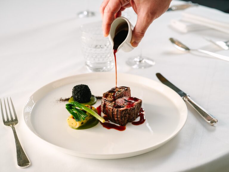 Sauce poured over a plated meat main course on a white tablecloth, Cliveden House