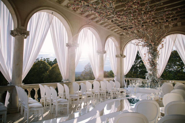 An arcaded loggia hung with white drapes and set with white chairs and a mirrored table, looking out over the valley, Cliveden House