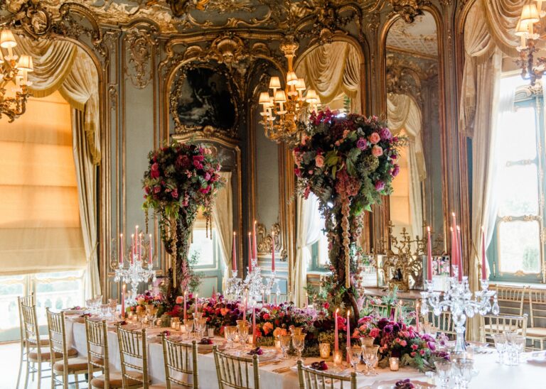 The gilded French Dining Room laid for a wedding dinner with tall floral centrepieces and candelabra, Cliveden House