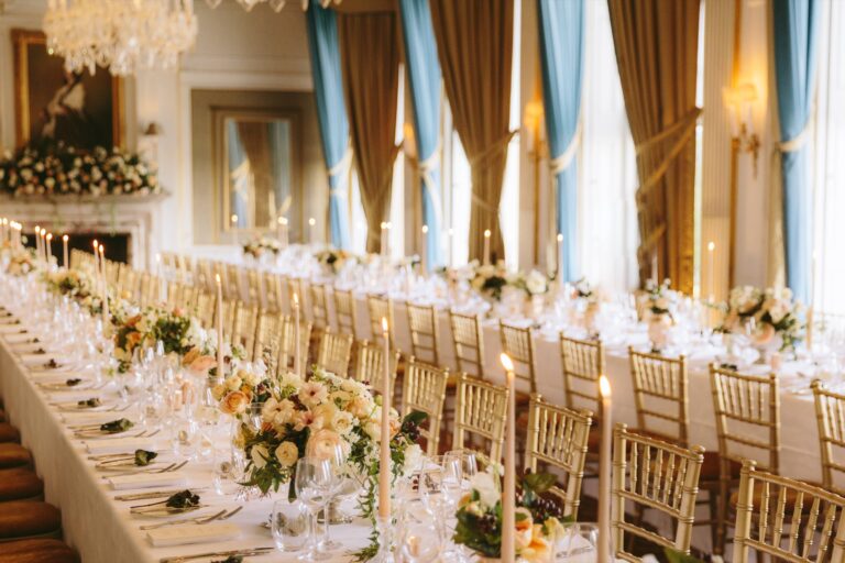 Long tables with gold chairs, taper candles and peach roses beside tall windows in The Cliveden Dining Room, Cliveden House