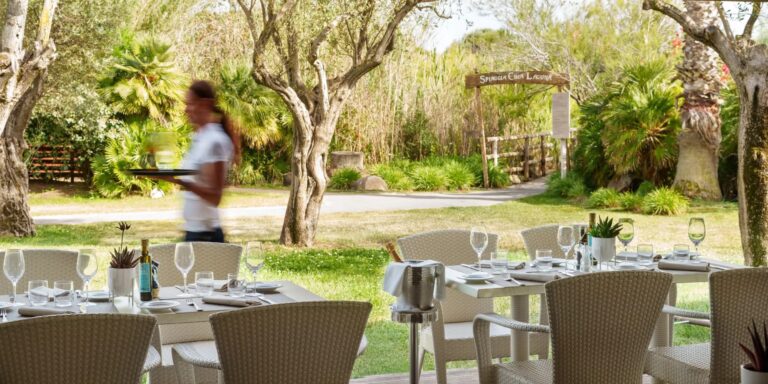 Tables laid in the garden at Le Dune, the resort restaurant near the beach, under trees and palms, Conrad Chia Laguna Sardinia