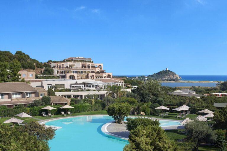 The Conrad's Laguna building above a pool and gardens, with Chia Tower and the sea behind, Conrad Chia Laguna Sardinia