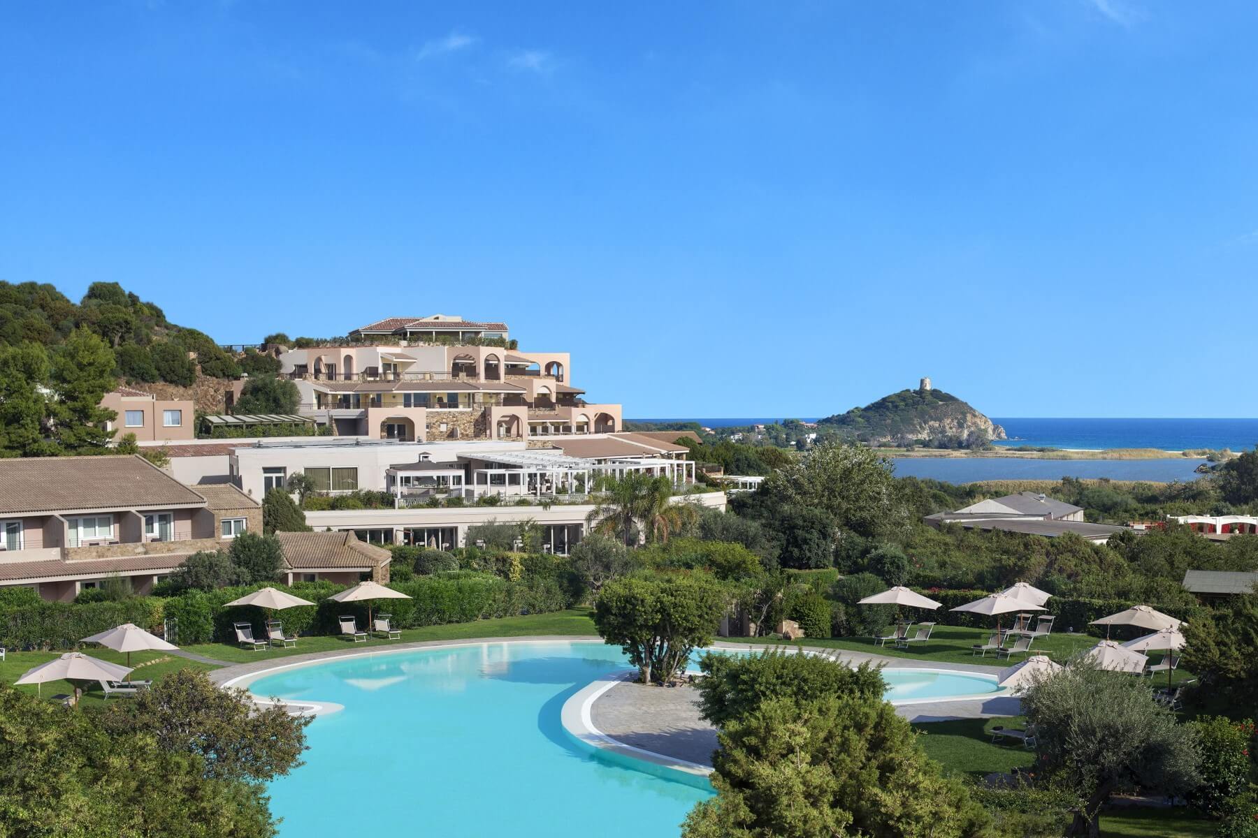 The Conrad's Laguna building above a pool and gardens, with Chia Tower and the sea behind, Conrad Chia Laguna Sardinia