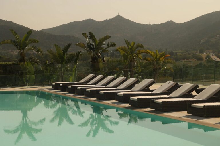 Loungers along a pool with palms and the hills behind in evening light, Conrad Chia Laguna Sardinia
