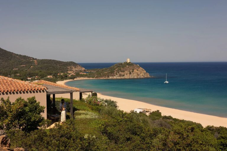 Rows of parasols on a wide beach backed by dunes, with a lagoon behind, Conrad Chia Laguna Sardinia