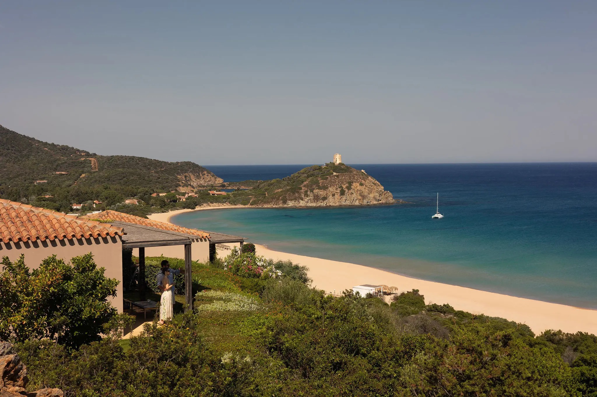 Rows of parasols on a wide beach backed by dunes, with a lagoon behind, Conrad Chia Laguna Sardinia