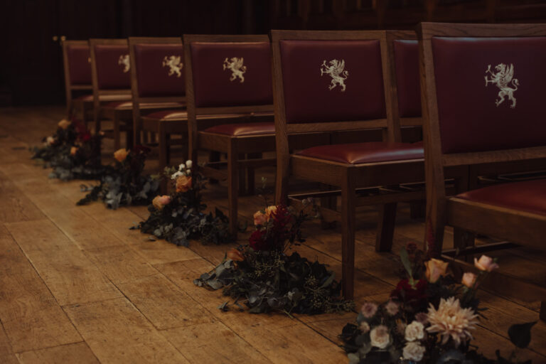 Red leather chairs carved with a lion crest, with dark flowers along the aisle on a wooden floor, Gray's Inn