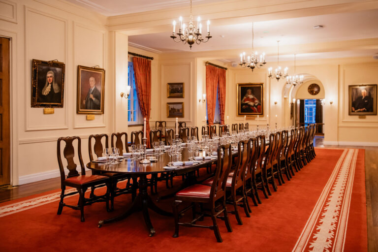 A long dining table laid in the Large Pension Room under chandeliers and portraits, Gray's Inn