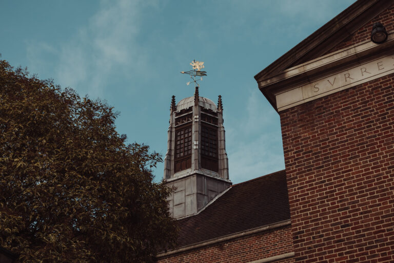 A stone tower with a weathervane rising beside a red-brick building, against a blue sky, Gray's Inn