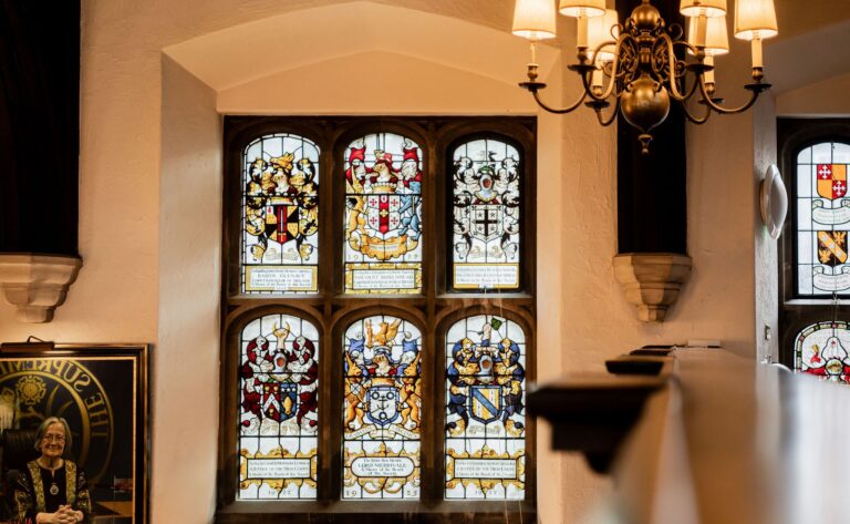 Heraldic stained glass in a window of the Hall, beside a brass chandelier, Gray's Inn