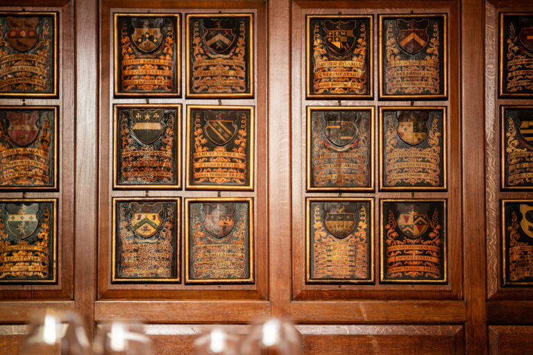 Painted coats of arms set into the oak panelling above a table laid for dinner, Gray's Inn