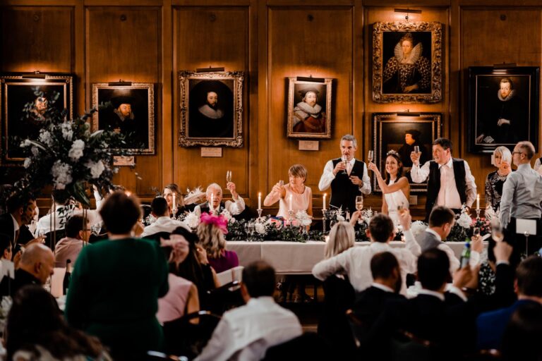 Wedding guests raising their glasses at dinner in the panelled Hall, under rows of portraits, Gray's Inn