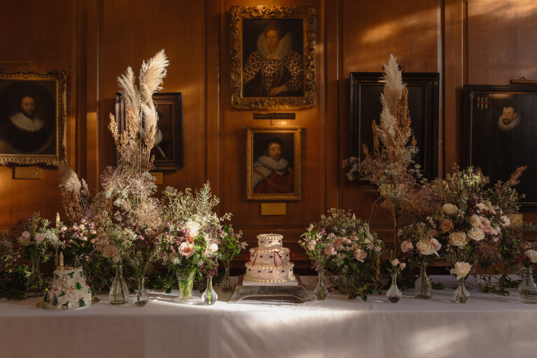 A wedding cake between dried-flower arrangements on a table before portraits on oak panelling, Gray's Inn