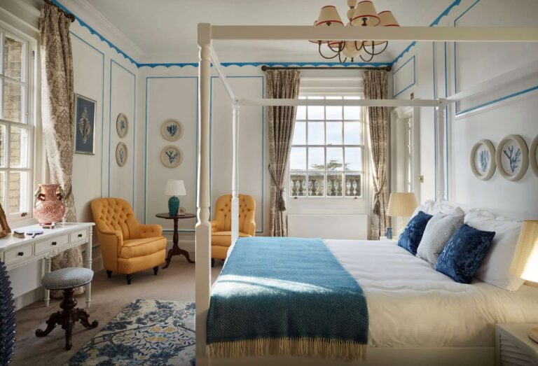 The Capri Suite, with a white four-poster, blue trim and yellow armchairs, Hedsor House