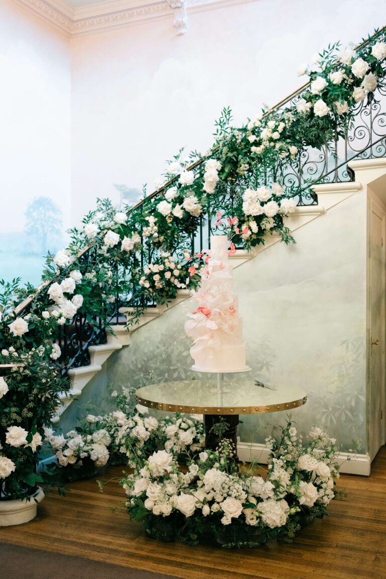 A staircase garlanded with white roses, with the wedding cake on a table at its foot, Hedsor House
