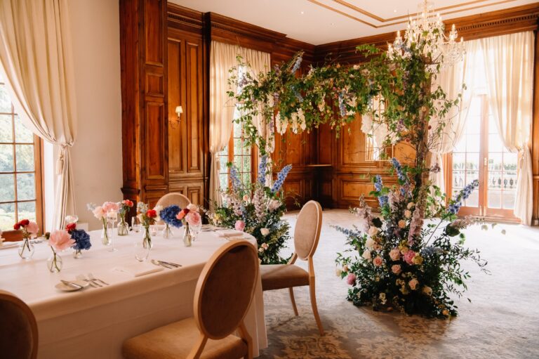 A top table in the Ballroom with low posies and a tall floral installation by the windows, Hedsor House