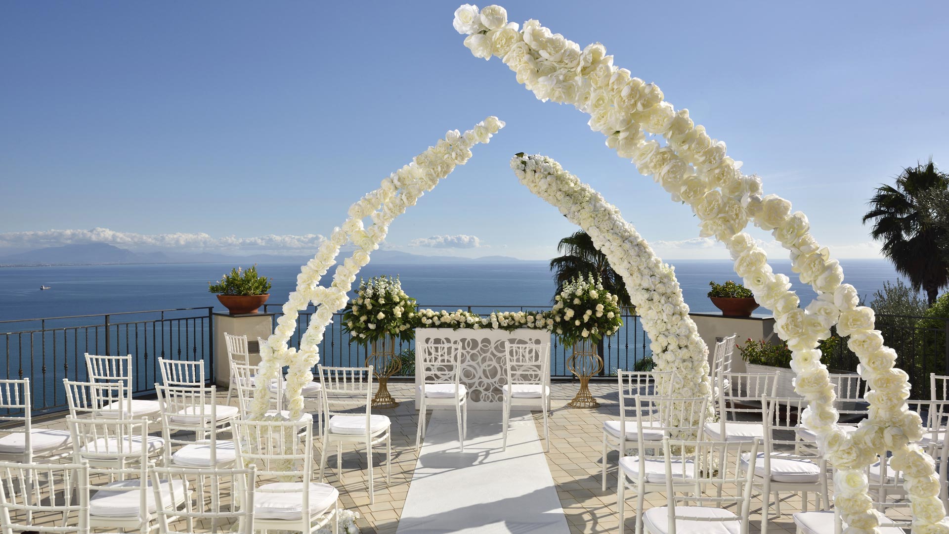 A floral arch and rows of white chairs on a terrace facing the gulf, Hotel Raito